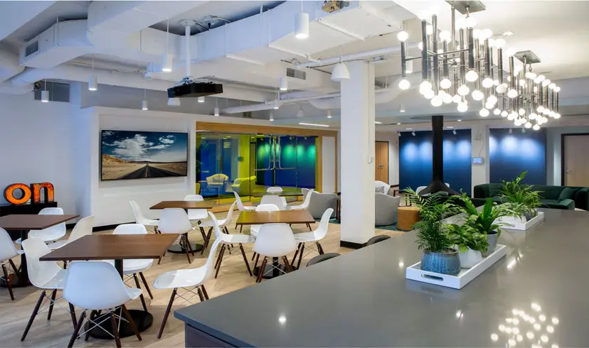 Modern coworking lounge with communal tables, kitchen area, and collaborative workspace seating