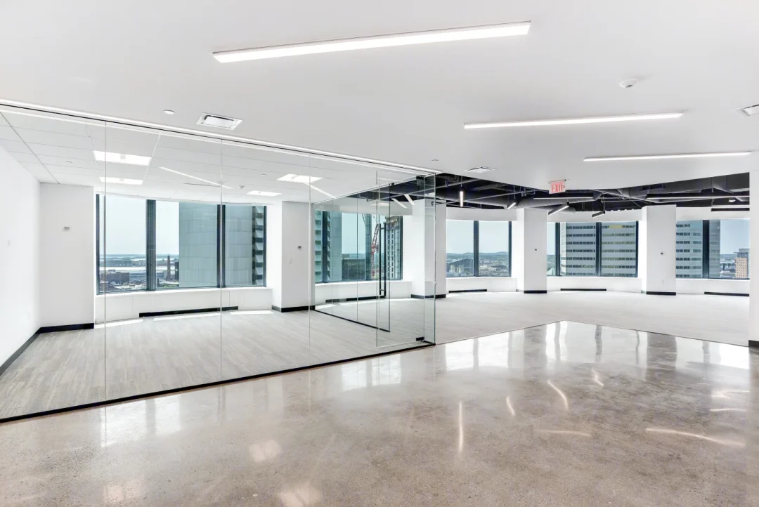 Bright, open office interior featuring glass partitions, polished concrete floors, and floor-to-ceiling windows with skyline views.