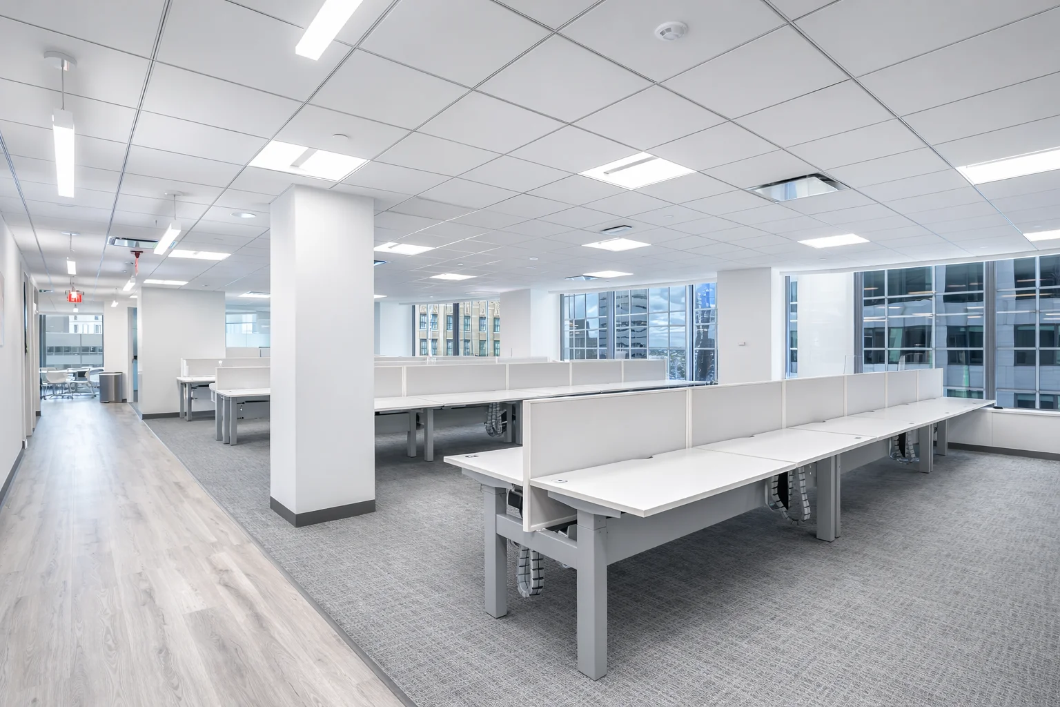 Modern open office workspace with shared desks, natural light, and city view windows