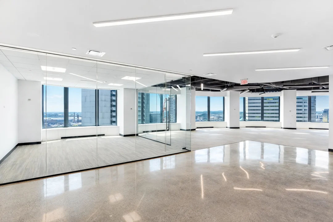 Modern high-rise office interior featuring glass partitions, polished concrete floors, and floor-to-ceiling windows overlooking downtown buildings.