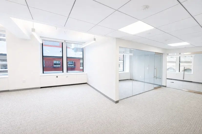 Bright, vacant office interior featuring neutral carpeting, glass conference room, and natural light from large windows.